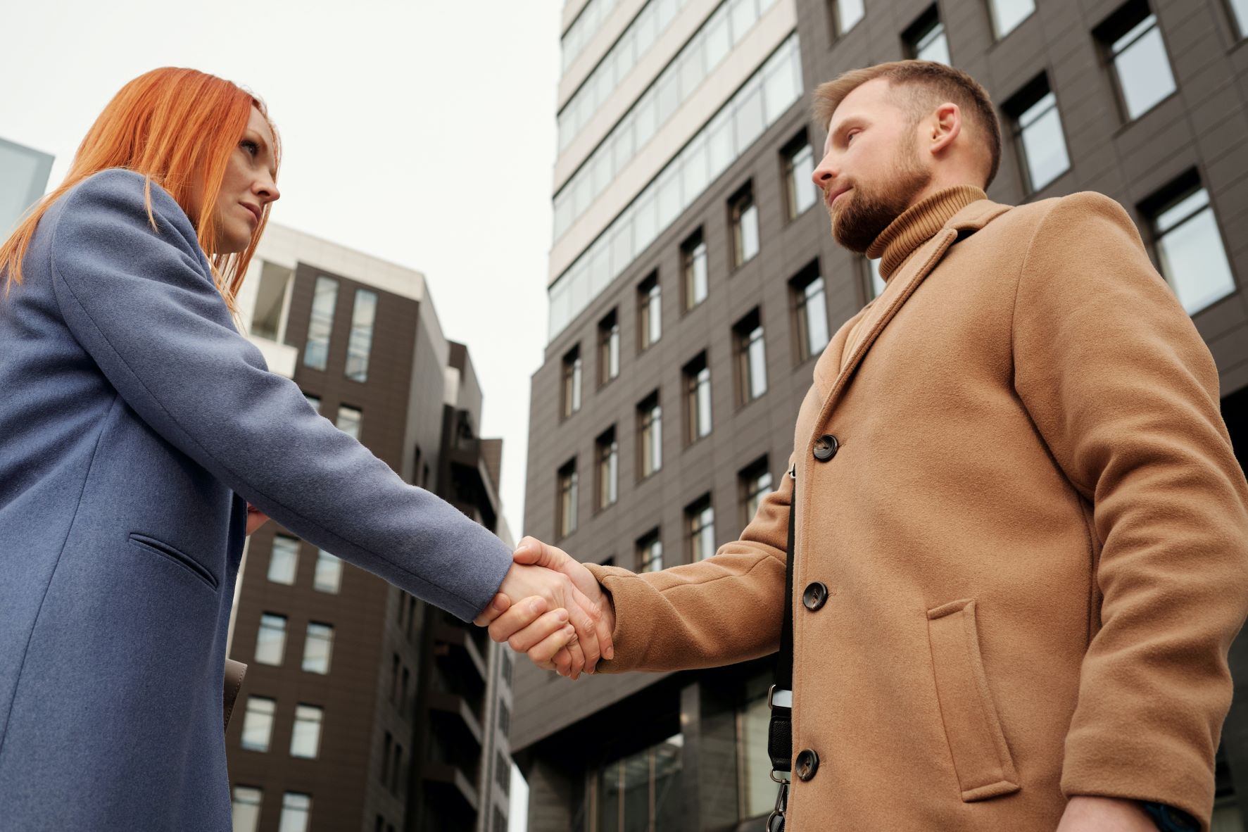 Un homme et une femme se serrent la main devant des immeubles